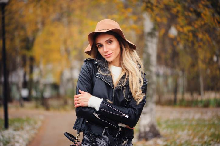 fashion autumn portrait of young happy woman walking outdoor in fall park in hat and leather jacket