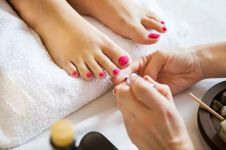 Woman in nail salon receiving pedicure by beautician